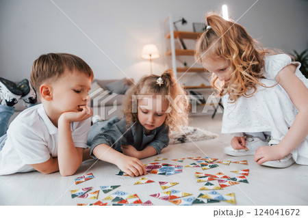Sitting on the floor and playing game. Group of children is together at home at daytime Sitting on the floor and playing game. Group of children is together at home at daytime 124041672
