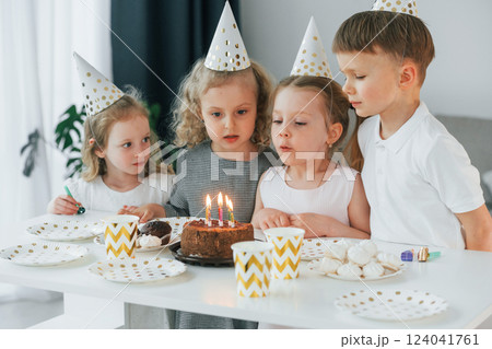Sitting by the table with cake. Celebrating birthday. Group of children is together at home at daytime 124041761