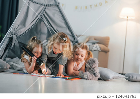 Laying down in the tent with flashlight and pencils to draw. Group of children is together at home at daytime 124041763