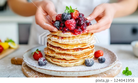 Chef garnishing stack of pancakes with berries and icing sugar Chef garnishing stack of pancakes with berries and icing sugar 124041956