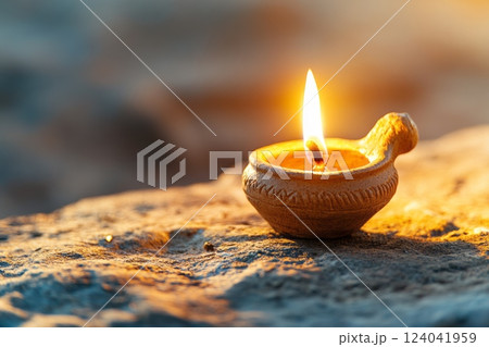Burning clay oil lamp illuminating stone at sunset, symbol of hope and remembrance 124041959