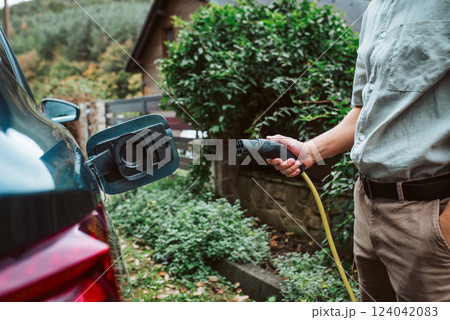 Man charging electric car, plugging charger in charging port. Man charging electric car, plugging charger in charging port. 124042083