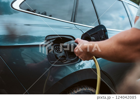 Man charging electric car, plugging charger in charging port. Man charging electric car, plugging charger in charging port. 124042085