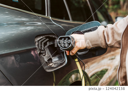 Man charging electric car, hodding charger in hand. Man charging electric car, hodding charger in hand. 124042138