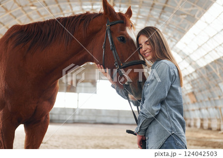 Young woman in jeans clothes is with horse on a stable 124042503
