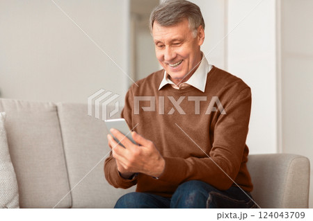 Mobile App. Joyful Senior Gentleman Using Cellphone Texting Sitting On Sofa Indoor. Selective Focus, Copy Space 124043709
