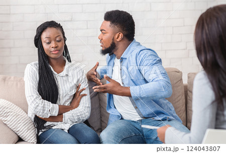 Anxious black man blaming his indifferent wife during therapy counselling session, emotionally gesturing while sitting on couch in counselor's office. Anxious black man blaming his indifferent wife during therapy counselling session, emotionally gesturing while sitting on couch in counselor's office. 124043807
