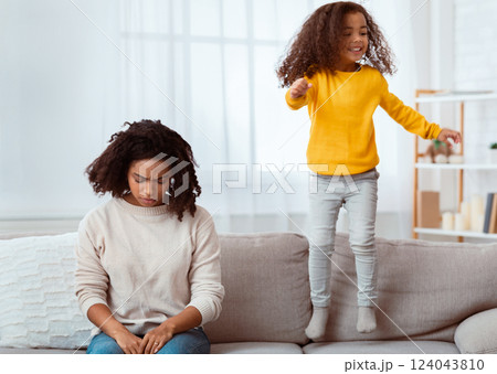 Parenting Hyperactive Kid. Exhausted Black Mother Sleeping While Daughter Jumping On Sofa At Home Parenting Hyperactive Kid. Exhausted Black Mother Sleeping While Daughter Jumping On Sofa At Home 124043810