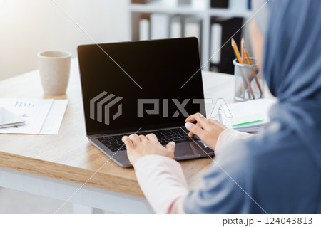 Unrecognizable muslim woman working on laptop with black screen, typing on keyboard, sitting in modern office, over shoulder view, mockup Unrecognizable muslim woman working on laptop with black screen, typing on keyboard, sitting in modern office, over shoulder view, mockup 124043813