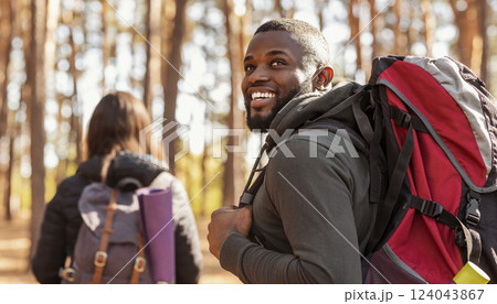 Happy black guy with backpack looking aside, hiking with girlfriend at forest 124043867