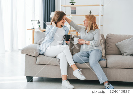 Talking with each other. With cups of drink in hands. Mother and daughter is together at home 124043927