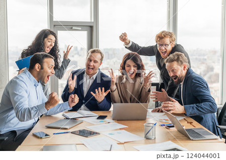 A team of five business professionals, dressed in suits and business casual attire, gather around a conference table in an office setting. They are all excitedly celebrating a success A team of five business professionals, dressed in suits and business casual attire, gather around a conference table in an office setting. They are all excitedly celebrating a success 124044001