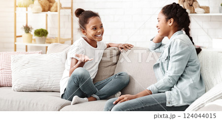 Two lovely african sisters having conversation at home, sitting on sofa at living room, copy space 124044015