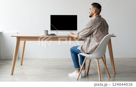 Rear Back View Of Happy Smiling Arab Man Looking At Pc Computer With Blank Black Screen For Mock Up Template Sitting At Desk At Home Office, Free Copy Space. People, Technology, Remote Work Concept Rear Back View Of Happy Smiling Arab Man Looking At Pc Computer With Blank Black Screen For Mock Up Template Sitting At Desk At Home Office, Free Copy Space. People, Technology, Remote Work Concept 124044016