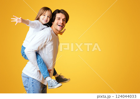 Cheerful Funny Father Playing With His Happy Little Girl, imitating airplane, yellow background, panorama with empty space Cheerful Funny Father Playing With His Happy Little Girl, imitating airplane, yellow background, panorama with empty space 124044033