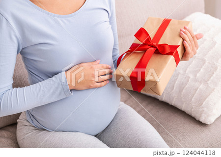 Unrecognizable Pregnant Lady Holding Wrapped Gift Box Sitting On Couch At Home. Cropped 124044118
