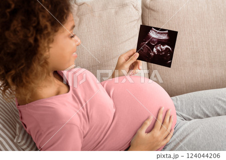 African-american pregnant woman holding ultrasound scan, relaxing on couch African-american pregnant woman holding ultrasound scan, relaxing on couch 124044206