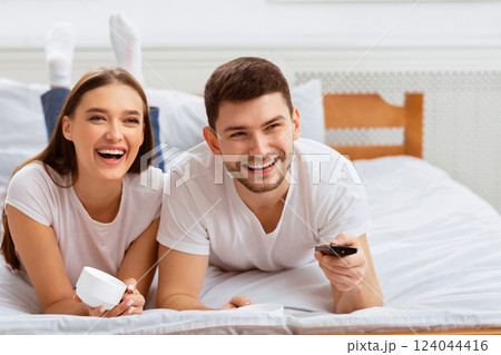 Weekend Leisure. Happy Couple Watching TV Relaxing Together Lying In Bed Indoor. Selective Focus, Free Space Weekend Leisure. Happy Couple Watching TV Relaxing Together Lying In Bed Indoor. Selective Focus, Free Space 124044416