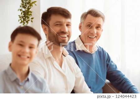 Happy Elderly Man With Middle-Aged Son And Grandson Smiling At Camera Sitting On Couch At Home. Selective Focus 124044423