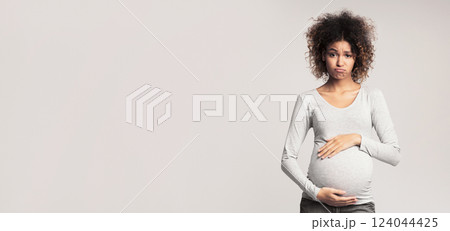 Hormones and mood changes. Sad expectant woman touching belly over grey studio background 124044425