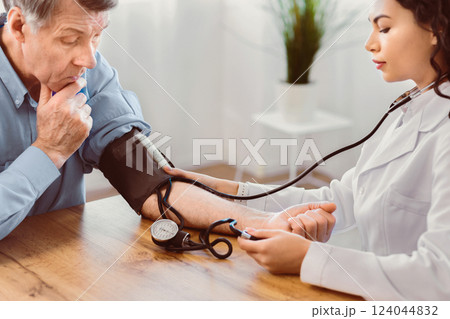 Cardiology. Mexican nurse measuring blood pressure of elderly man with hypertensive crisis at clinic office, copyspace Cardiology. Mexican nurse measuring blood pressure of elderly man with hypertensive crisis at clinic office, copyspace 124044832