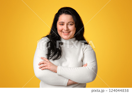 Body Positive. Young Plus Size Model Girl Posing With Folded Arms Over Yellow Background And Smiling At Camera Body Positive. Young Plus Size Model Girl Posing With Folded Arms Over Yellow Background And Smiling At Camera 124044838