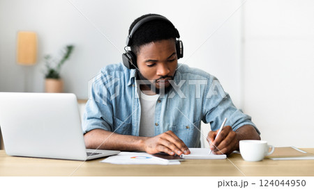 Concentrated african american guy in headphones studying foreign language online through video conference and making notes in notebook, panorama with copy space Concentrated african american guy in headphones studying foreign language online through video conference and making notes in notebook, panorama with copy space 124044950