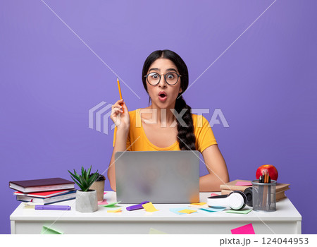 Idea Concept. Excited Young Indian Woman In Eyeglasses Sitting At The Desk Using Laptop And Raising Pencil Up Isolated Over Purple Background In Studio. Amazed Shocked Lady Having Insight, Aha Moment. 124044953