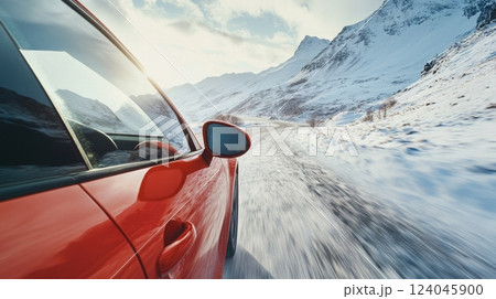 A red car speeds along a narrow, winding road surrounded by majestic snowy mountains under a sunset sky. The landscape captures the essence of winter and adventure, highlighting the beauty of nature. 124045900