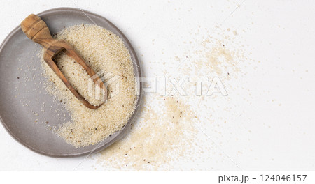 Raw uncooked fonio seeds on grey plate with a wooden scoop on white table topview. African cereal Raw uncooked fonio seeds on grey plate with a wooden scoop on white table topview. African cereal 124046157