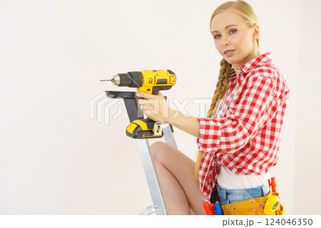 Woman on ladder using drill Woman on ladder using drill 124046350