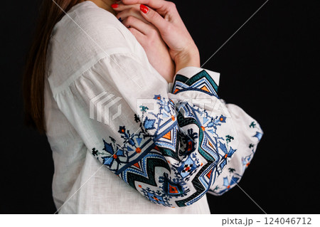 Close-up View of Intricately Embroidered Sleeve on Traditional White Blouse Against Black Background 124046712