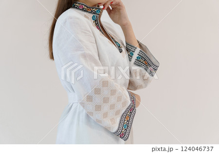 Elegant Woman Wearing White Dress with Intricate Colorful Embroidery on Sleeves and Collar Against Plain Background 124046737