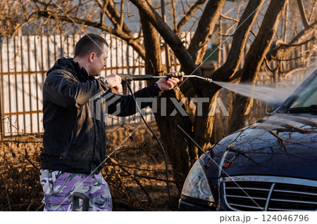 Man Cleaning Dark Blue Car with High-Pressure Water Spray Outdoors on Sunny Day 124046796