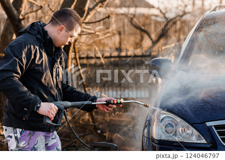 Man Carefully Washing Car with Pressure Washer Outdoors in Autumn Setting 124046797