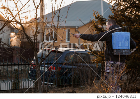 Man Spraying Trees in Garden with Backpack Sprayer During Sunset in Residential Area Man Spraying Trees in Garden with Backpack Sprayer During Sunset in Residential Area 124046813
