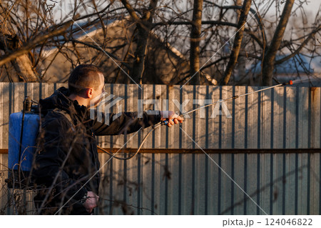 Man Holding Sprayer Spraying Chemicals onto Trees in Backyard During Sunset Man Holding Sprayer Spraying Chemicals onto Trees in Backyard During Sunset 124046822