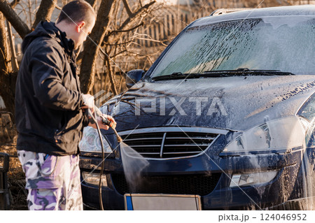 Man Cleaning Blue Car with High-Pressure Water Jet Outdoors on Sunny Day Man Cleaning Blue Car with High-Pressure Water Jet Outdoors on Sunny Day 124046952
