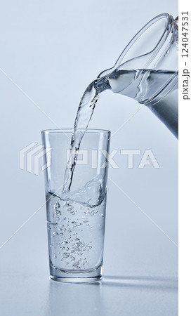 Close-up photo of transparent water being poured from pitcher into clear glass, showing bubbles, against soft blue background. Mock up. Close-up photo of transparent water being poured from pitcher into clear glass, showing bubbles, against soft blue background. Mock up. 124047531