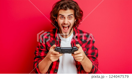 Excited young man plays video games in a vibrant red setting with a game controller in hand 124047579