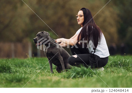 Sitting on the ground. Young brunette is having a walk with her dog outdoors Sitting on the ground. Young brunette is having a walk with her dog outdoors 124048414