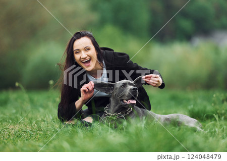 Playful mood. Holding by the ears. Young brunette is having a walk with her dog outdoors Playful mood. Holding by the ears. Young brunette is having a walk with her dog outdoors 124048479