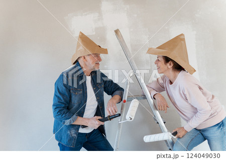 Portrait of senior couple having fun while painting walls with roller in new home. 124049030