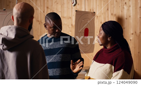 Shooting range safety officer ensuring clients are following regulations and operating firearms safely. African american firing range gallery worker giving instructions to customers, camera B Shooting range safety officer ensuring clients are following regulations and operating firearms safely. African american firing range gallery worker giving instructions to customers, camera B 124049090