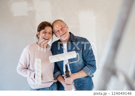 Senior couple painting walls with roller in new home, looking at camera. 124049146
