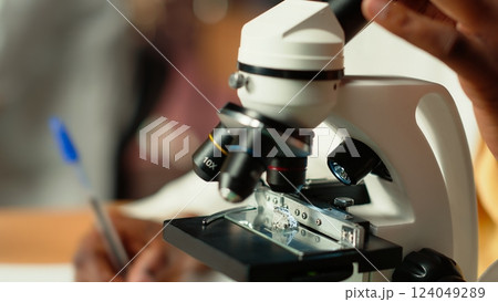 University student prepares for exam by researching cells and microorganisms under the microscope. Using books and papers from the academic database in the college library. Close up. Camera B. 124049289