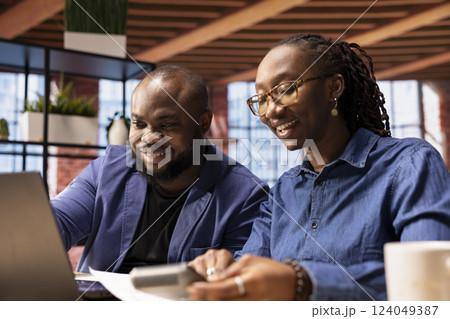 African american man and woman review their earnings and revenue reports in their apartment, using a calculator and laptop to ensure accurate accounting and financial planning for the tax season. 124049387