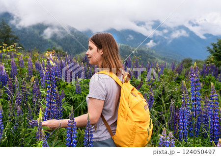 charming female traveler explores blooming meadow full of vibrant blue purple lupines lupine flowers, enjoying beauty of nature in the mountains, touching blossoming flowers, eco tourism 124050497