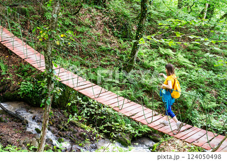 young woman in yellow backpack crosses narrow suspension bridge over rushing stream in lush green forest, concept of travel, trips, active lifestyle and overcoming obstacles, and life's difficulties young woman in yellow backpack crosses narrow suspension bridge over rushing stream in lush green forest, concept of travel, trips, active lifestyle and overcoming obstacles, and life's difficulties 124050498