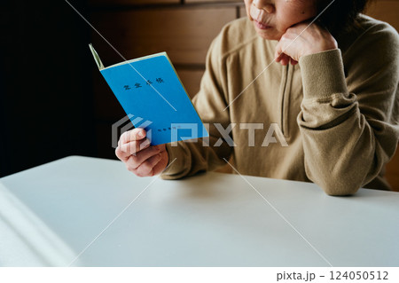 頬杖をついて年金手帳を見つめるシニア女性 124050512